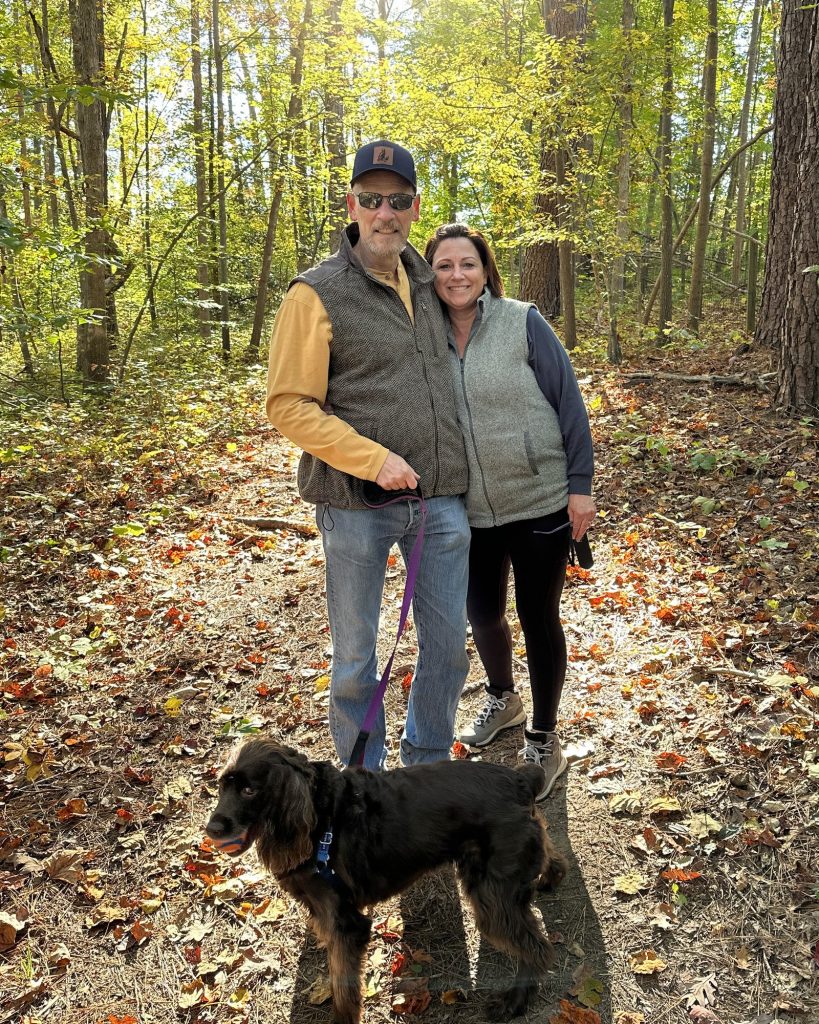 Leslie Brooks with her husband and their dog Dixie on a wooded trail in autumn