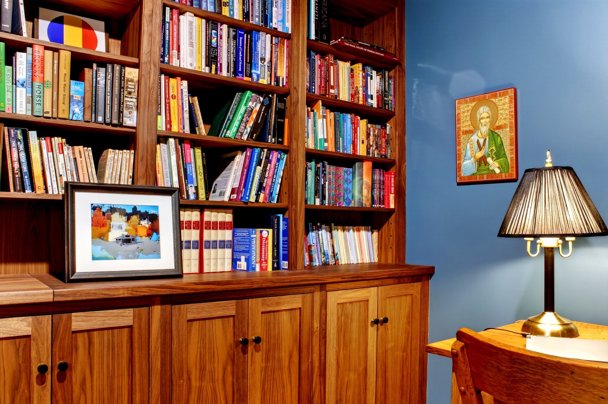 Library wall of built-in bookcases with a brass lamp and framed art