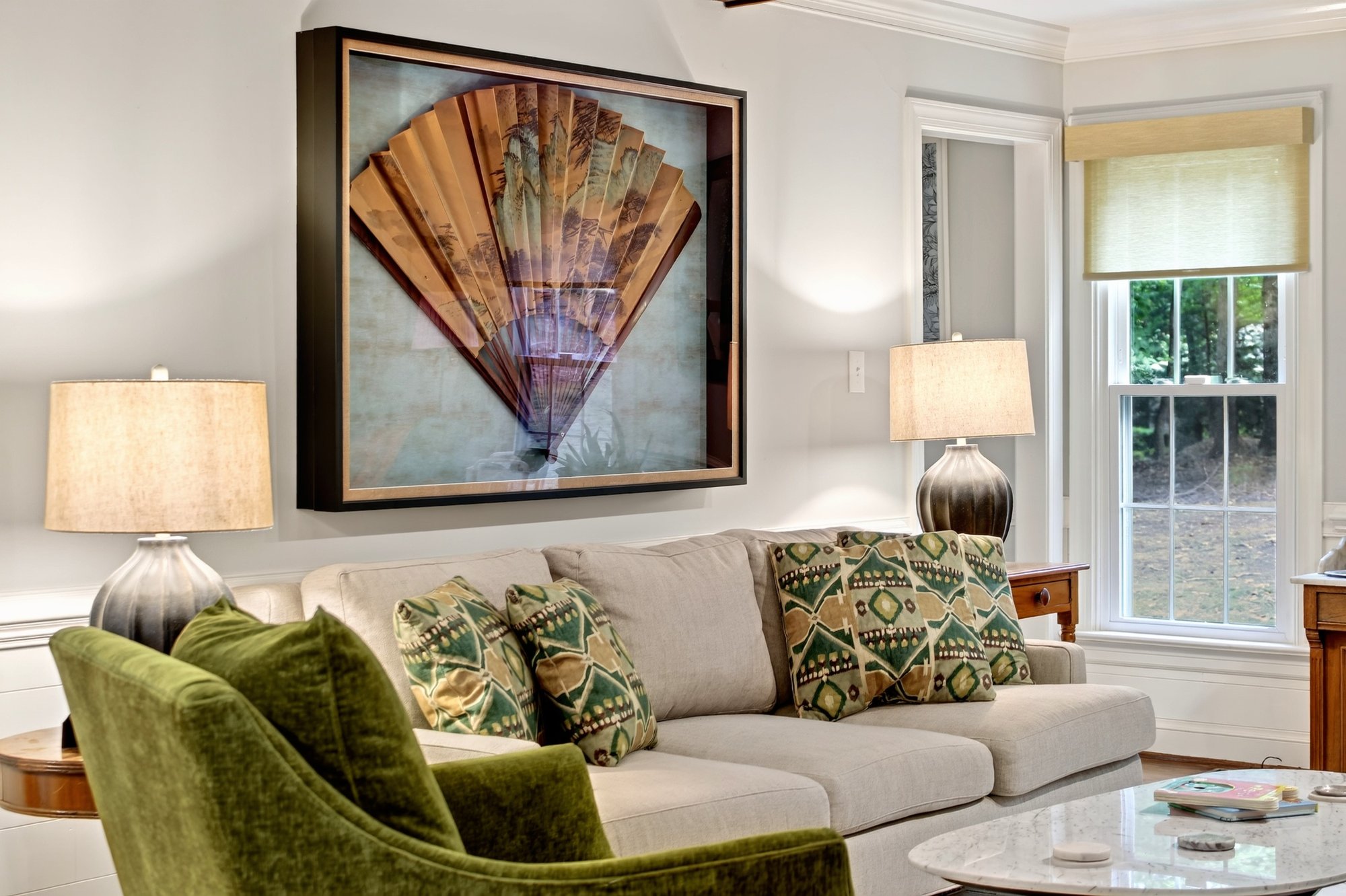 Living room with a fan-shaped artwork above the sofa and a pair of green armchairs
