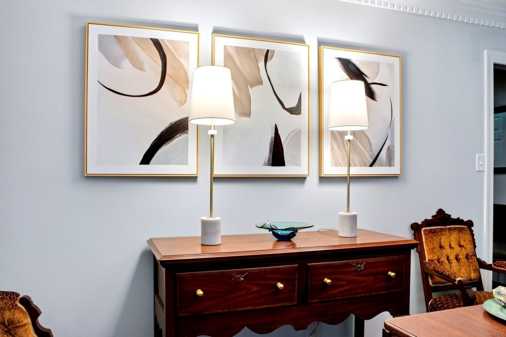 Sideboard beneath a three-panel artwork with a pair of table lamps